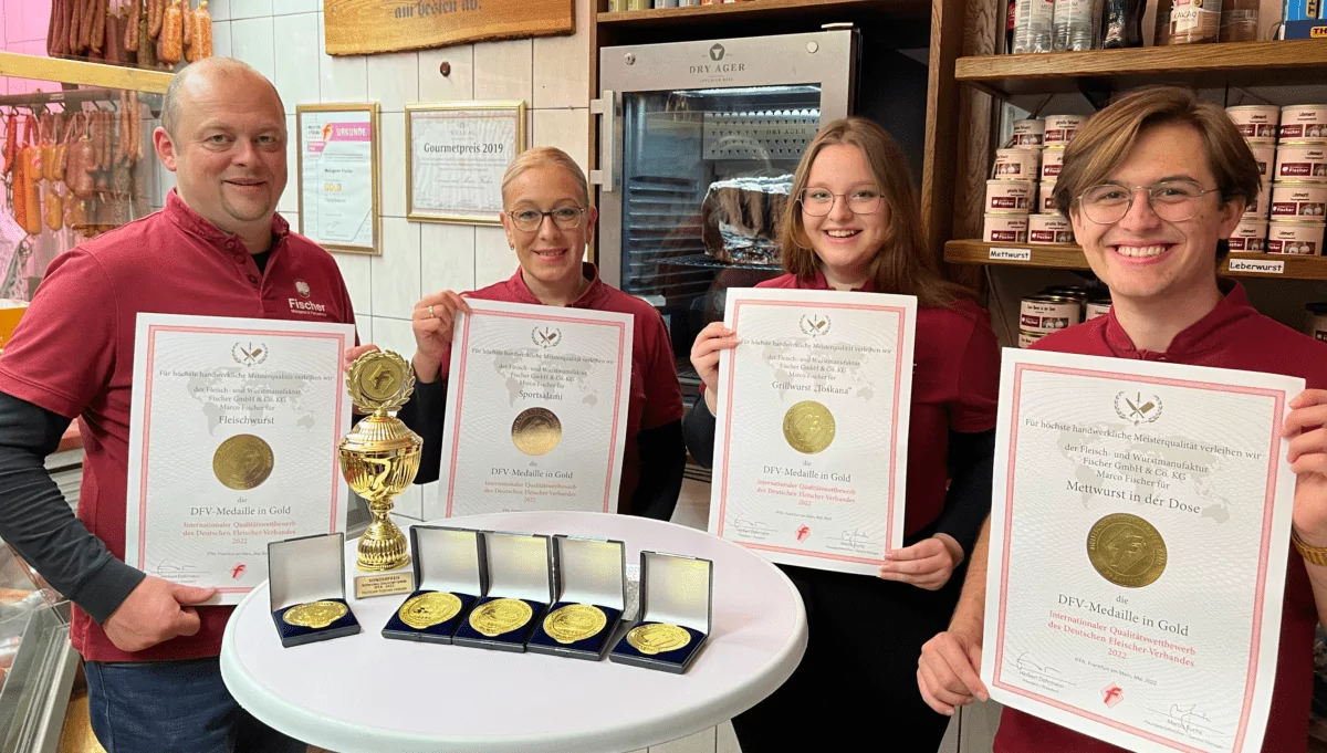 Vier Mitarbeiter zeigen goldene Metzgerei-Auszeichnungen und Medaillen