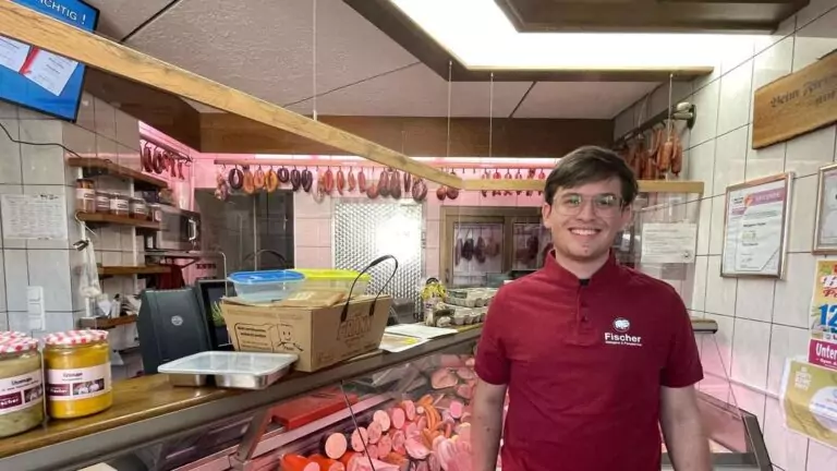 Lächelnder Metzger hinter Fleischtheke mit Wurstaufhängungen