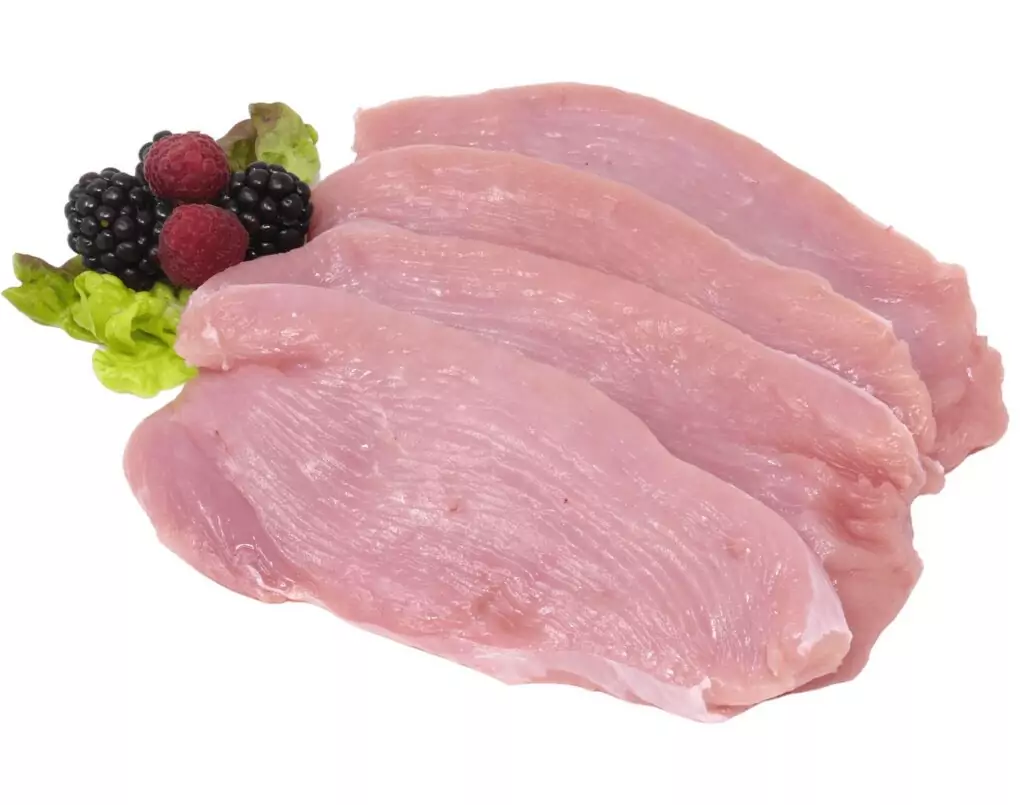 Drei rohe, dünne Putenbrustfilets auf weißen Hintergrund mit Brombeeren, Himbeeren und Blattsalat.