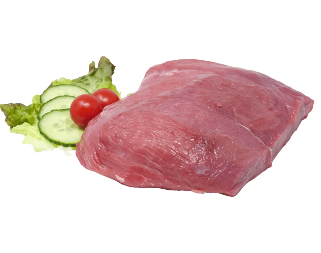 Rohes Stück rotes Fleisch auf Salatblättern mit Gurkenscheiben und kleinen roten Tomaten, vor weißem Hintergrund.